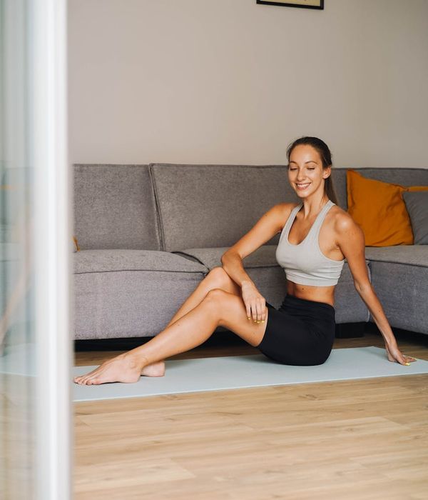 Smiling person stretching on a yoga mat in a sunlit room.